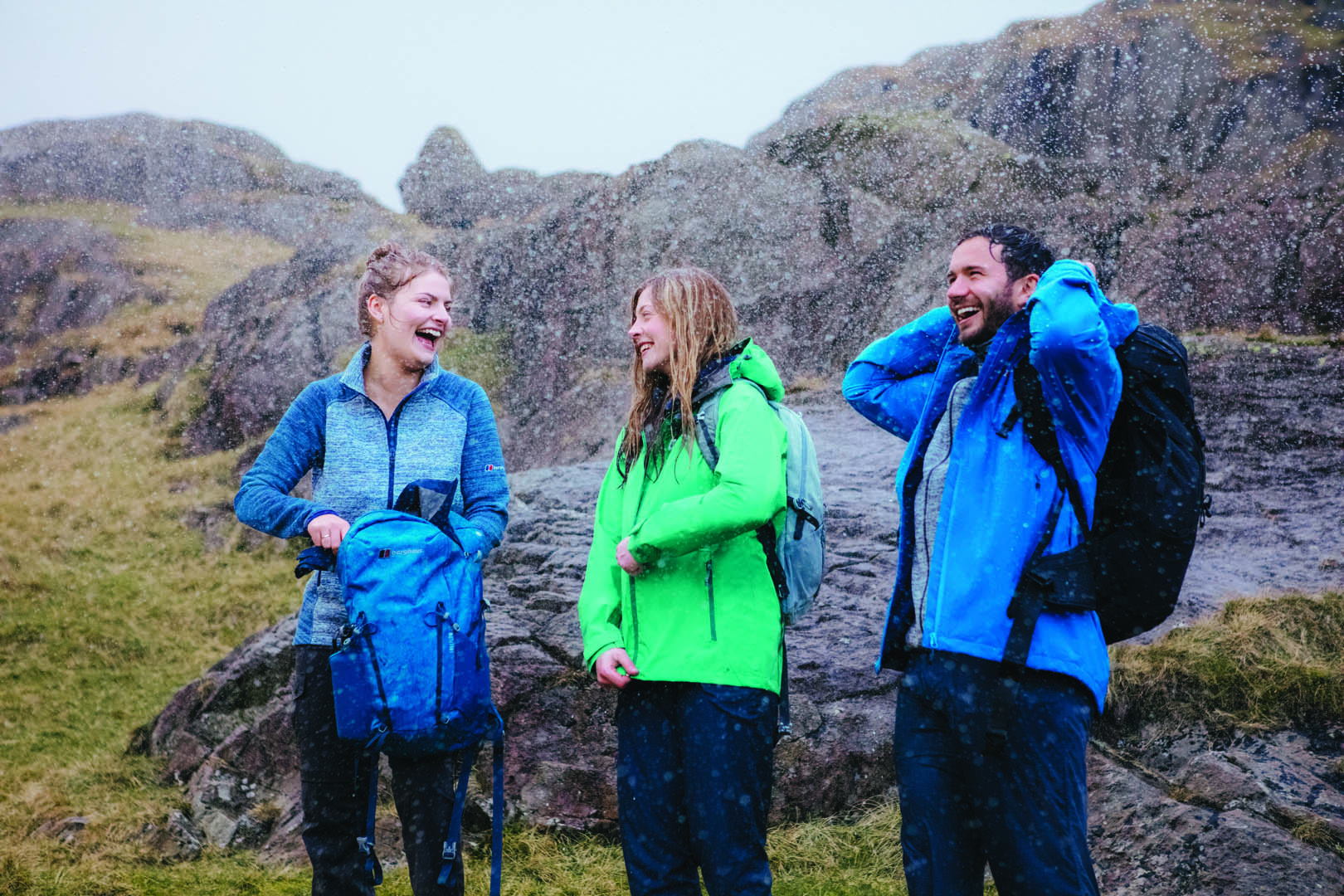 Drei Sportler von Berghaus stehen mit Berghaus Jacken und Rucksäcken in der Natur und es schneit